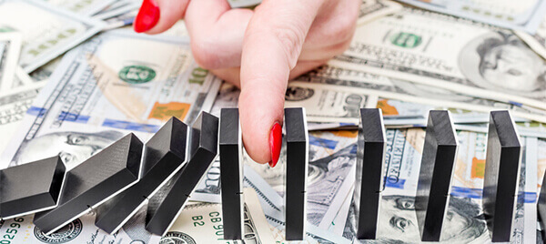Female hand stopping domino effect on dollar backgrounds. Business concept.